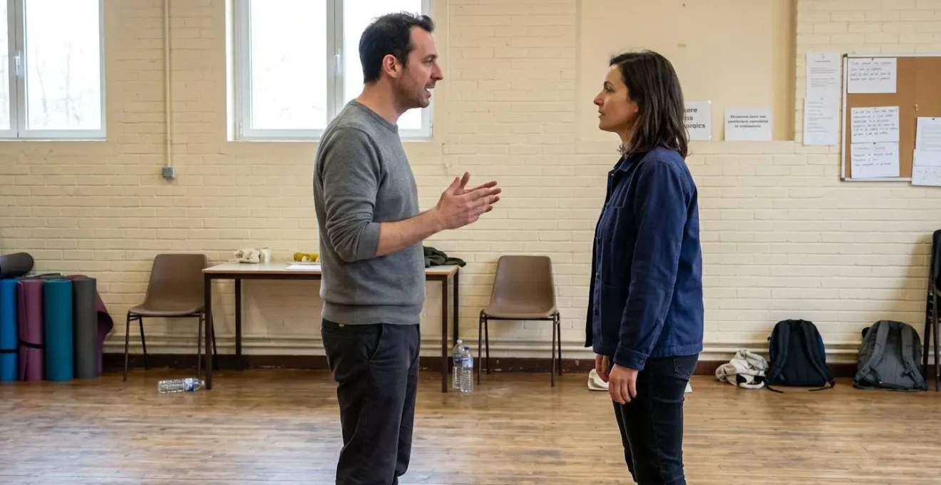 Deux adultes face à face lors d'un exercice théâtral dans une salle de répétition lumineuse, l'un gesticule naturellement en parlant